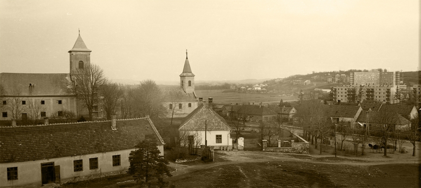 Ajka belvárosának látványa a Templomdombról az 1970-es évek elején. A fotó egyesített, felújított változatán jól látszik a kórház és az első panel épületek sziluettje, valamint a szölőhegy szinte üres oldala. / Ajkai Fotóklub, Sipos Ottó 